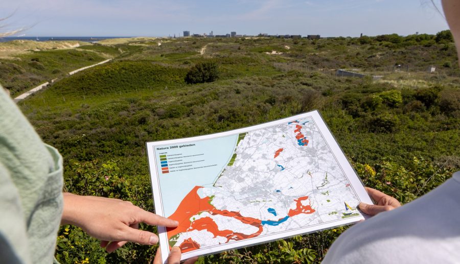 Een map van de Natura 2000-gebieden wordt vastgehouden op locatie in de duinen